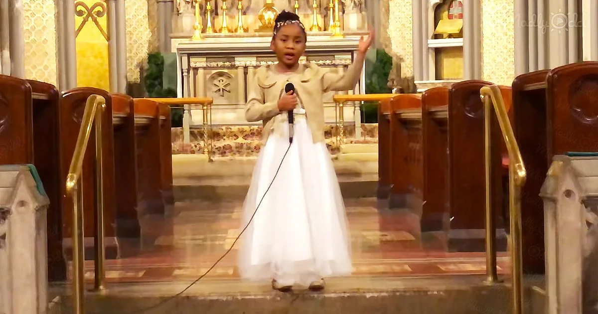 A young girl in a white dress sings into a microphone in a church.