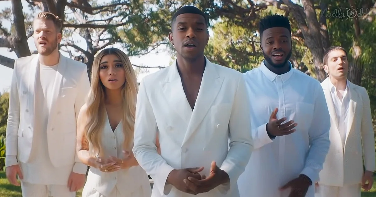 A man in a white suit stands center, surrounded by others in white, singing outdoors under trees.