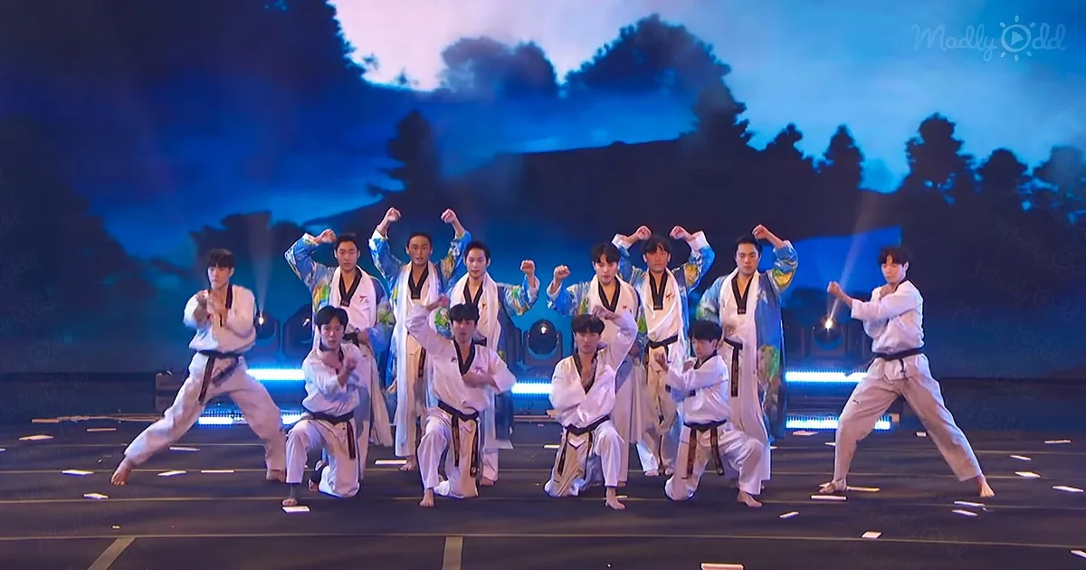 A group of performers in martial arts attire execute synchronized moves on a stage with a scenic backdrop.