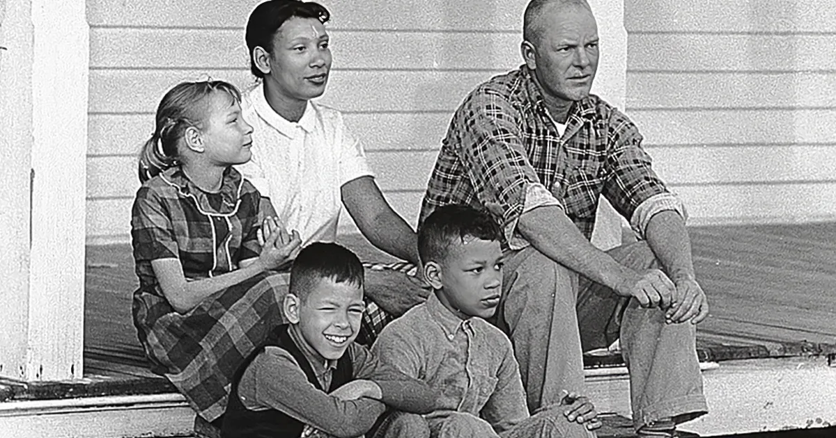 A family of five sits together on a porch, smiling and relaxed.