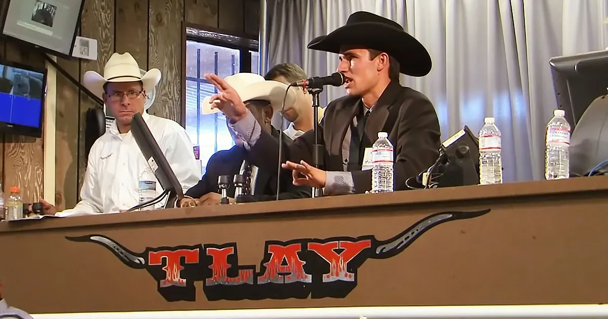 A man in a cowboy hat speaks into a microphone at a podium with "TLAY" and longhorns on it.