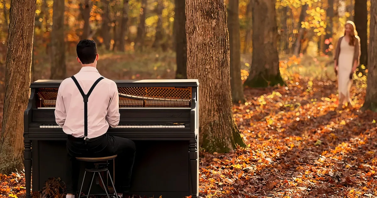 A man in suspenders plays a piano in a forest, while a woman in a white dress walks away.