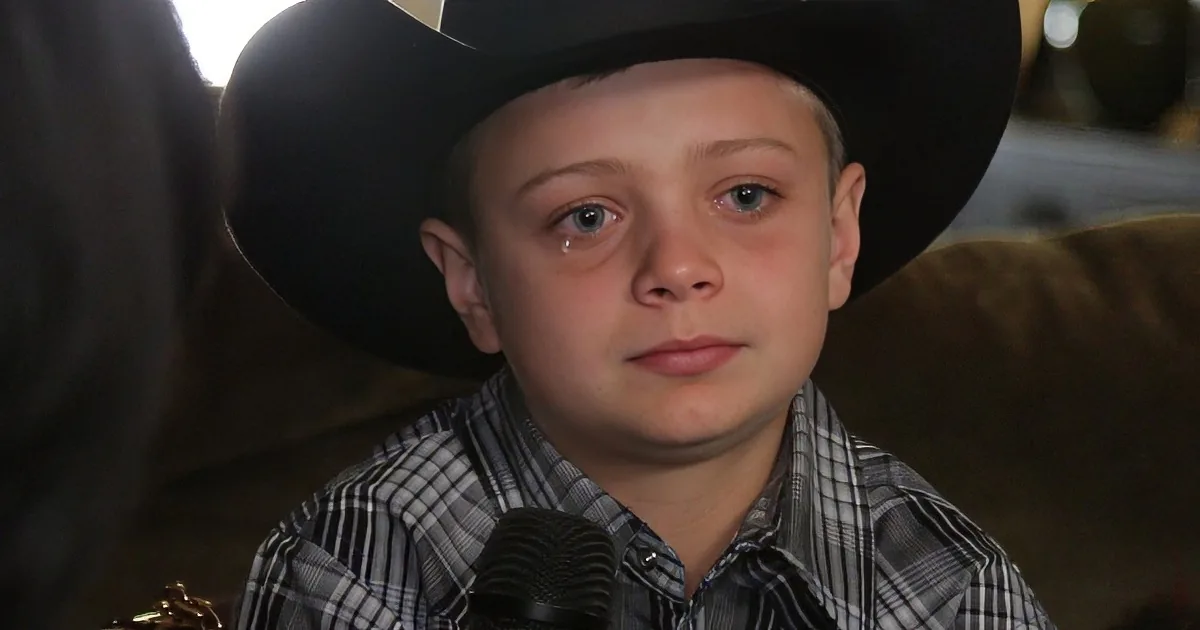 A young boy wearing a cowboy hat and plaid shirt looks concerned or sad.
