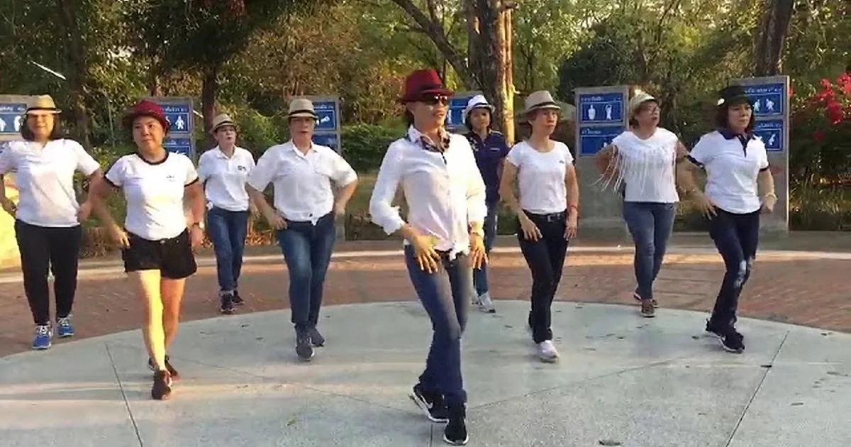 A group of people in white shirts and hats is dancing in a park.