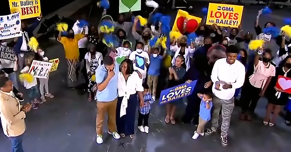 A group of people, including children and adults, cheer for Mr. Bailey with signs and pom-poms.