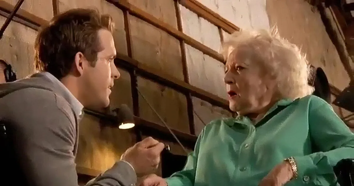 Ryan Reynolds and Betty White are seated, holding hands, smiling on a talk show set.