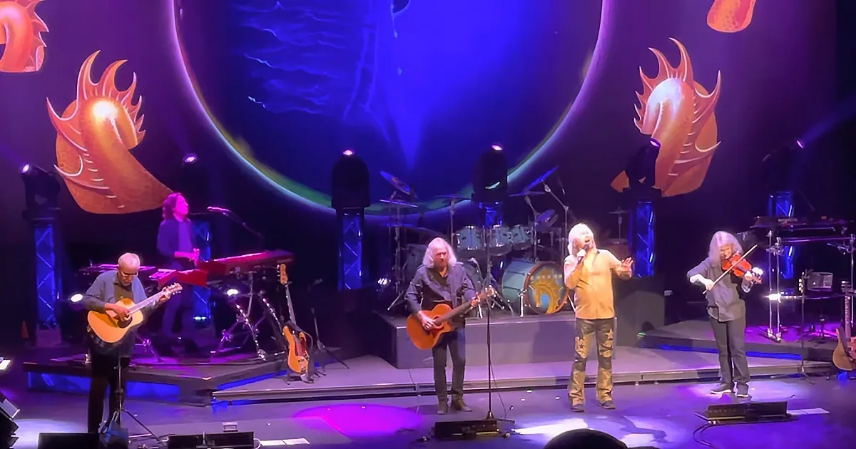 A band performs on stage with colorful lighting and a dragon-themed backdrop.