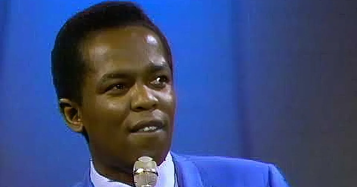 A man in a blue suit sings into a microphone on stage.