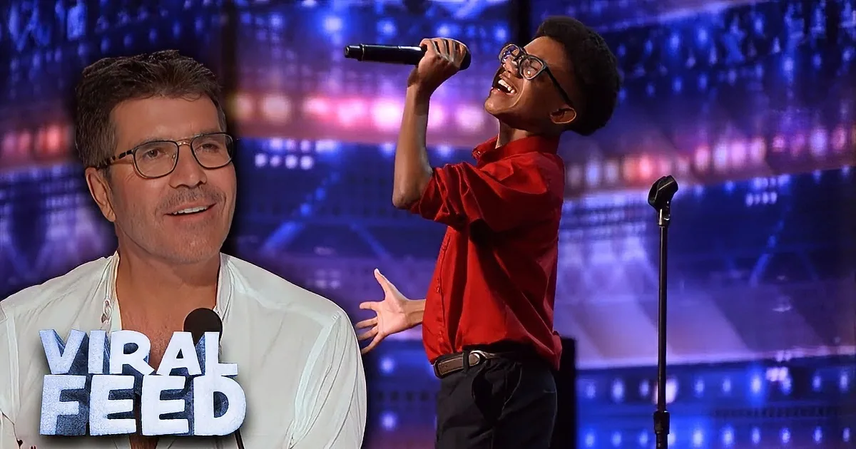A young man in a red shirt sings passionately on stage with a microphone, surrounded by a vibrant, colorful backdrop.