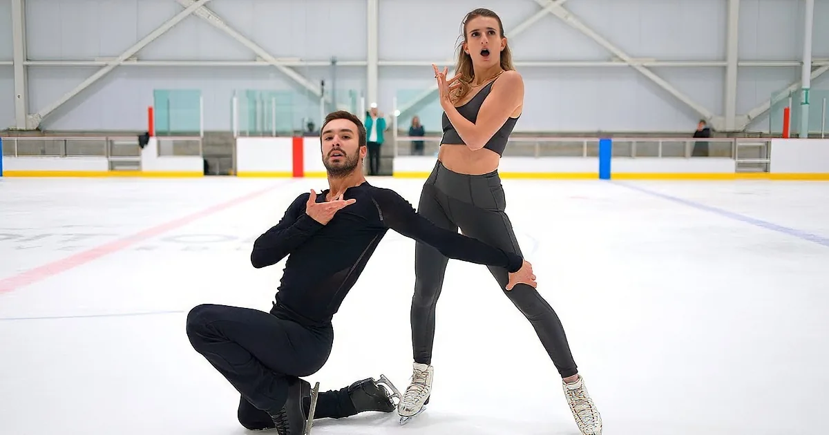 A couple in figure skating attire performs a synchronized move on an ice rink.