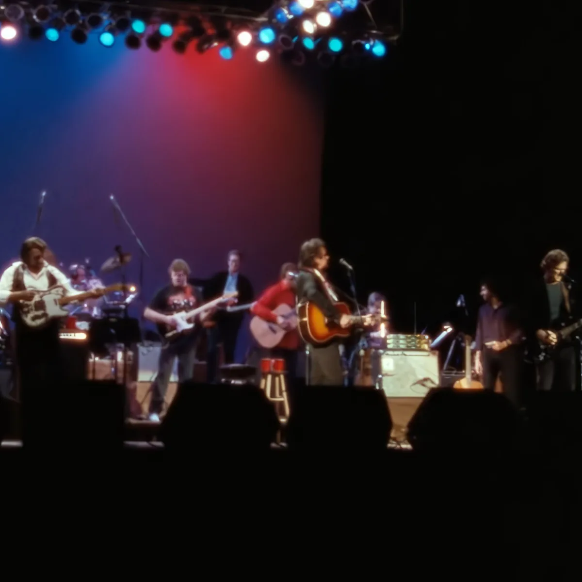 A band performs on stage with colorful lights, microphones, and instruments.