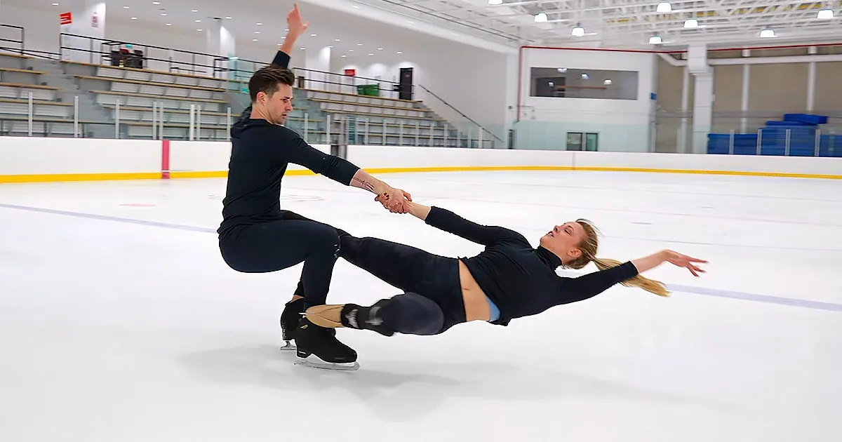 A figure skater in a dynamic pose, holding hands with a partner, gliding on an ice rink.