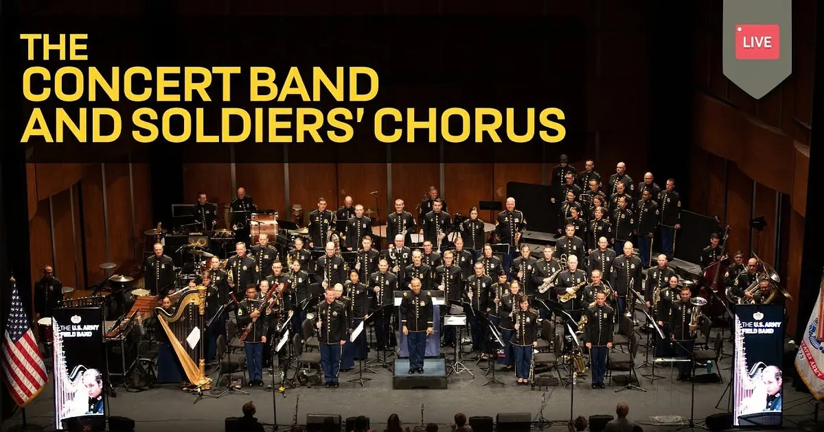 A military band in uniform plays instruments on stage with a choir and American flags in the background.