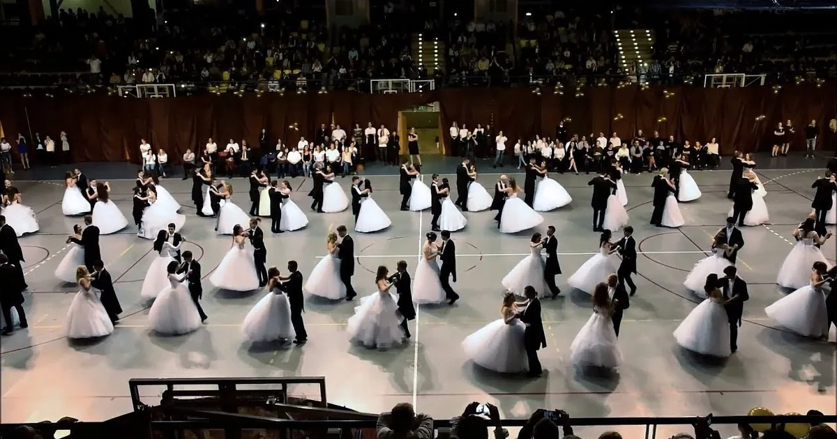 A ballet performance with dancers in white tutus and black suits on a basketball court.
