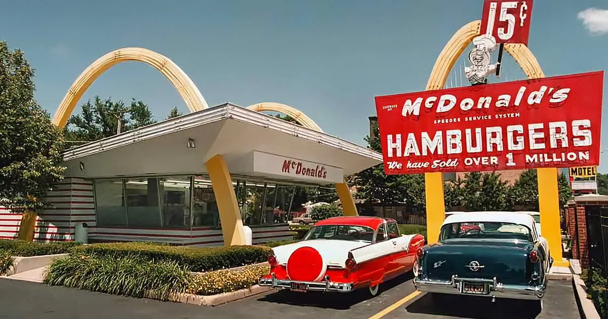 A vintage McDonald's restaurant with iconic golden arches, classic cars, and a sign boasting over 1 million hamburgers sold.