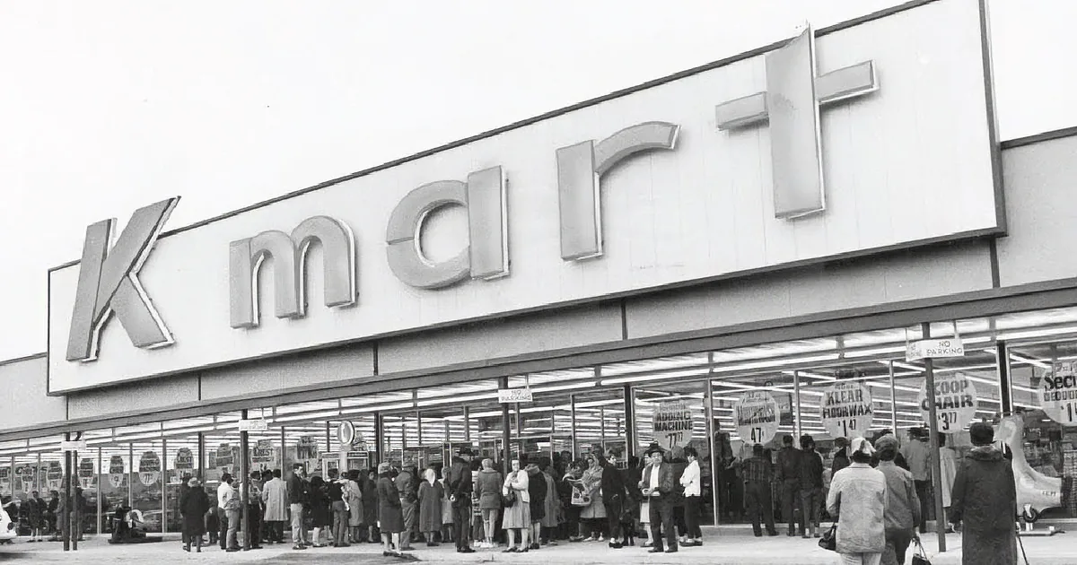 A Kmart store with a large sign, people standing outside, and sale signs displayed.