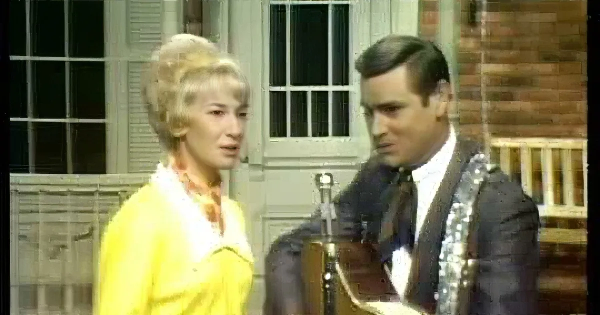 A woman in a yellow outfit sings into a microphone, accompanied by a man playing guitar.