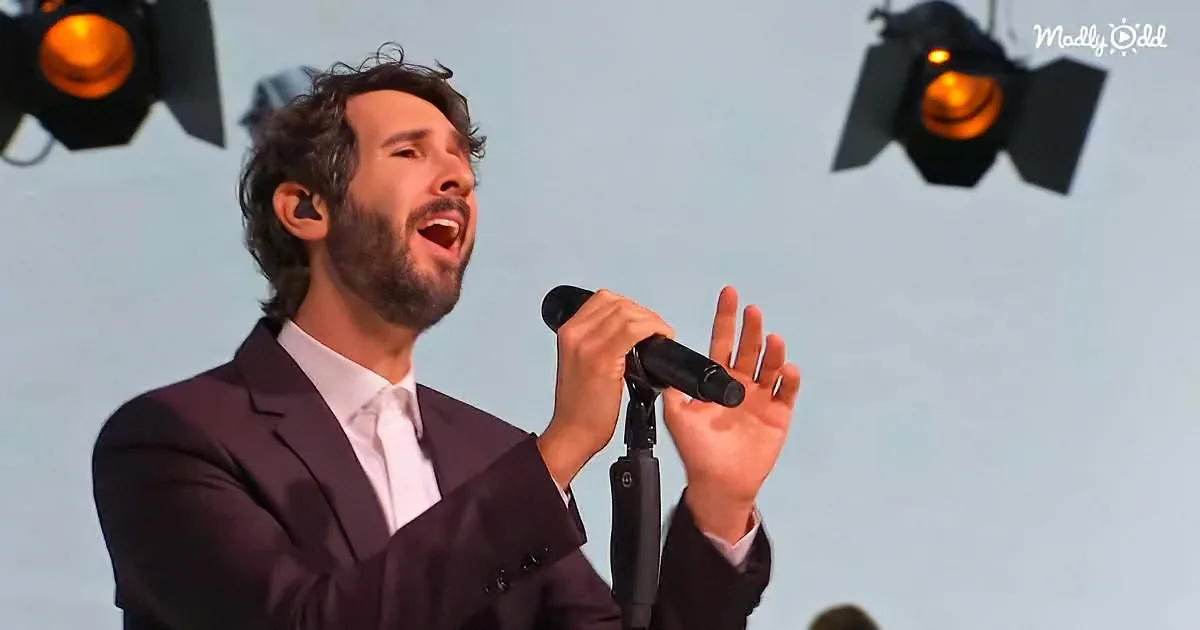 A man in a suit sings passionately into a microphone, illuminated by stage lights.