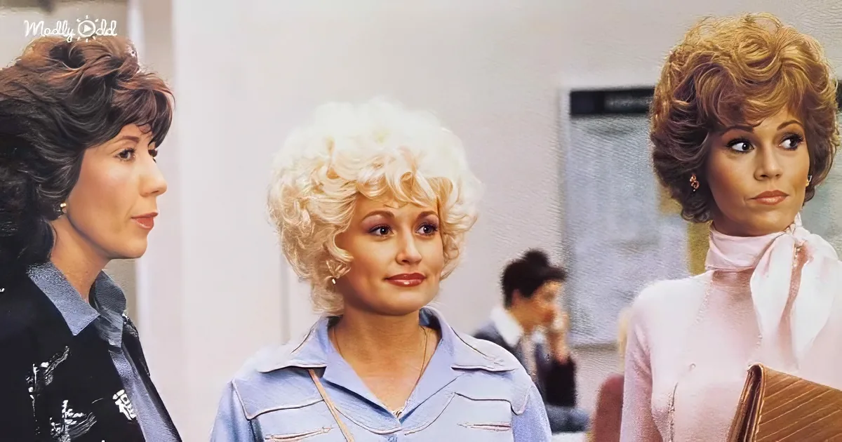 Dolly Parton, blonde curls, blue shirt, stands between two women, one in black, another in pink, in a room.