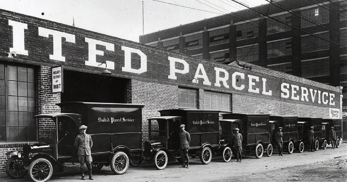 United Parcel Service trucks parked outside a brick building with workers standing nearby.