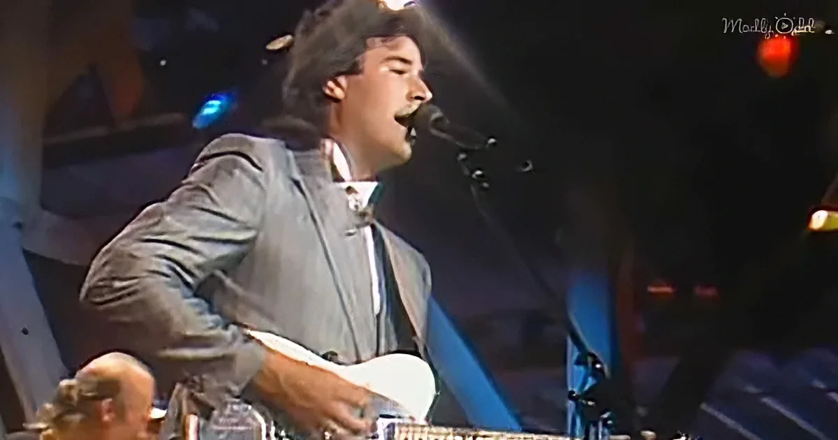A man in a suit plays guitar and sings into a microphone on stage.