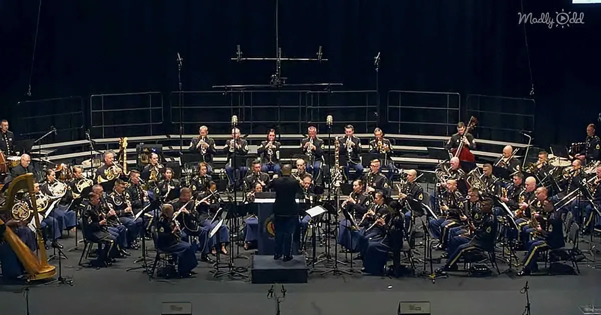 A military band in uniform plays instruments on stage under bright lights.