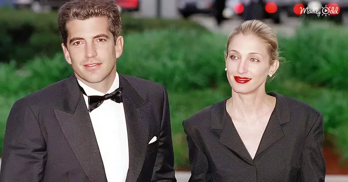 A man in a tuxedo and a woman in a black dress pose together, both looking directly at the camera.