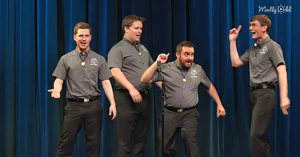Four men in matching uniforms perform on stage, smiling and gesturing.