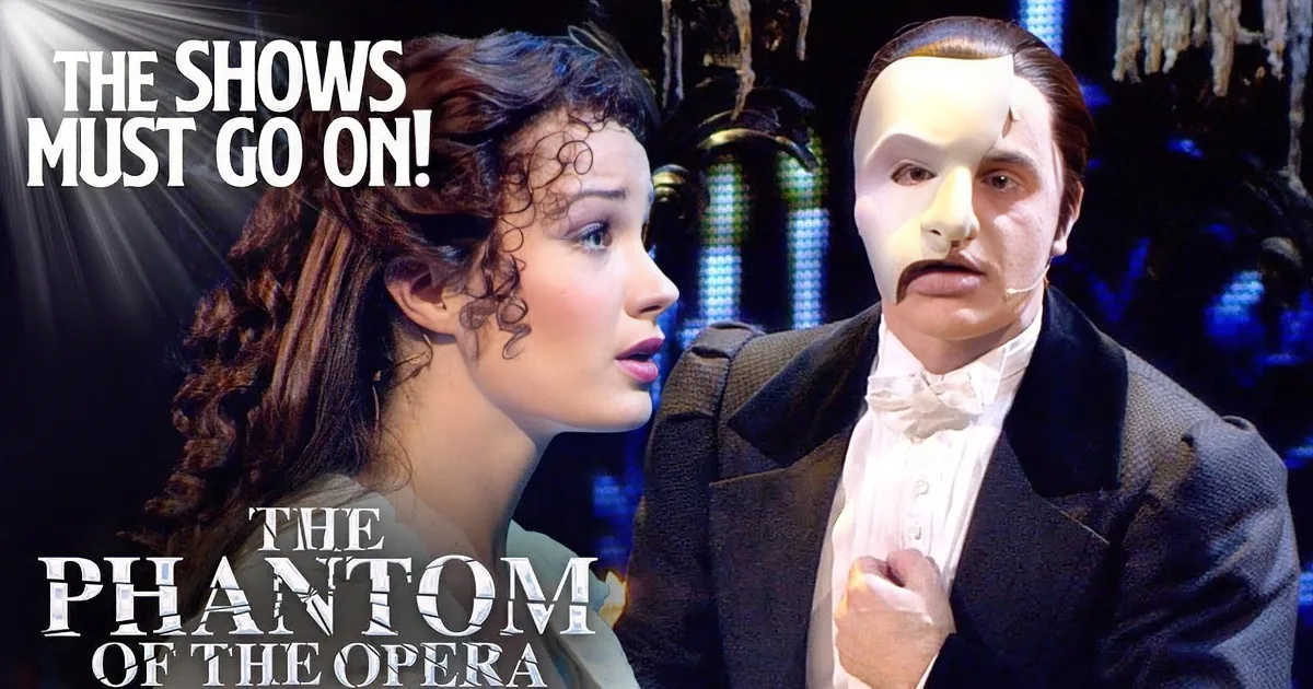 A man in a Phantom of the Opera mask gestures dramatically, holding a candle, while a woman with long hair looks on.
