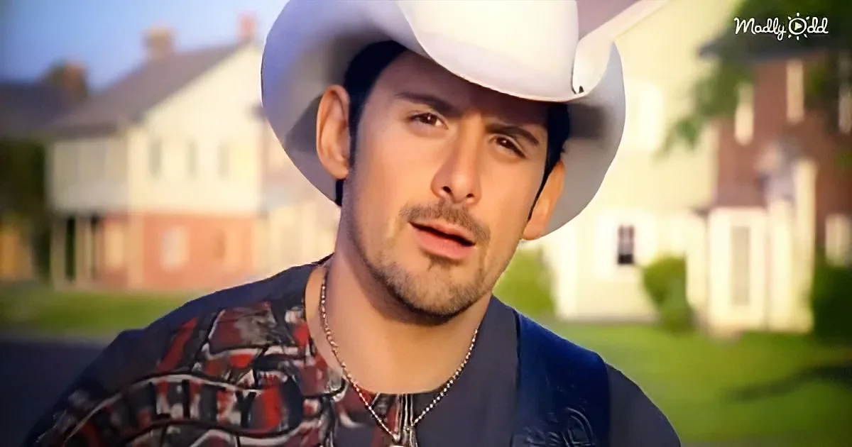 A man wearing a white cowboy hat and a patterned shirt stands in front of a blurred suburban background.