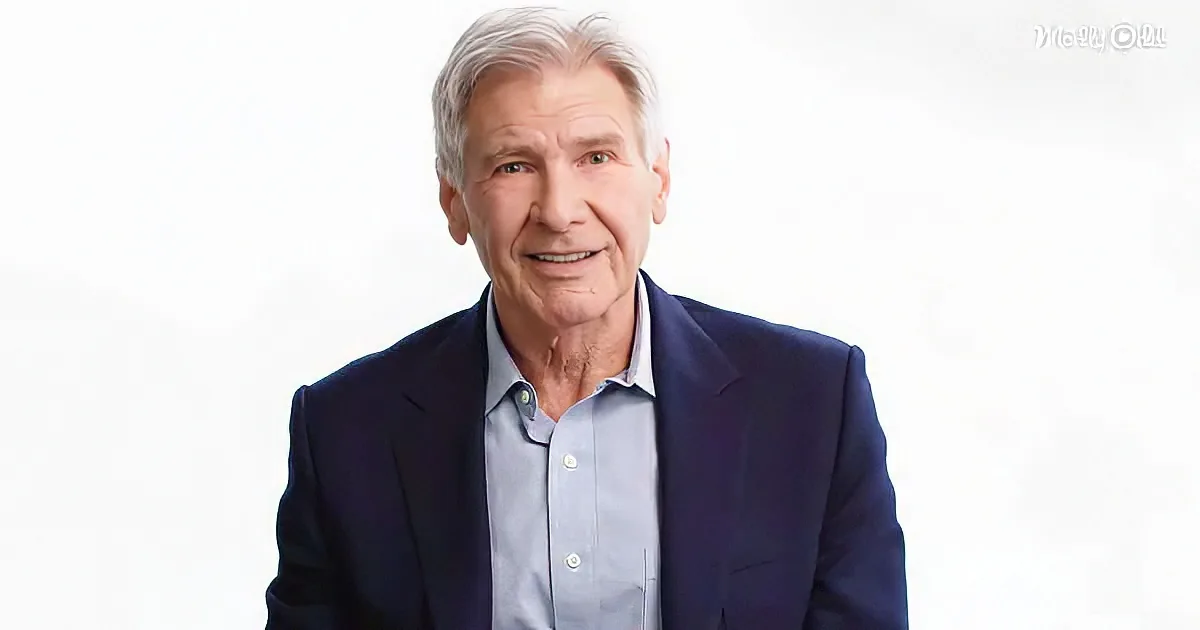 A man with gray hair, wearing a blue suit and light blue shirt, smiles against a white background.
