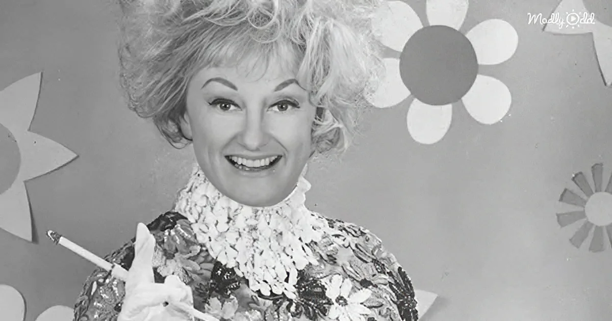 A woman with voluminous hair, wearing a floral outfit, holds a cigarette and napkin, smiling against a flower-patterned...