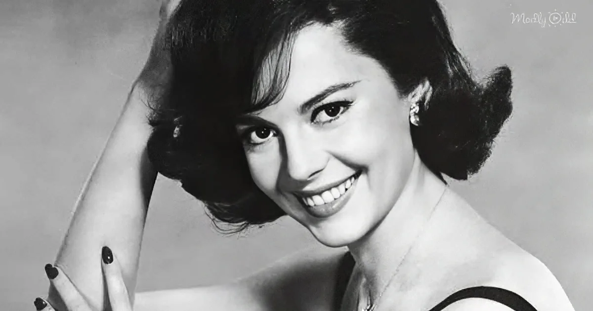 A smiling woman with dark hair in a bun, wearing a striped top and heart-shaped nail polish.