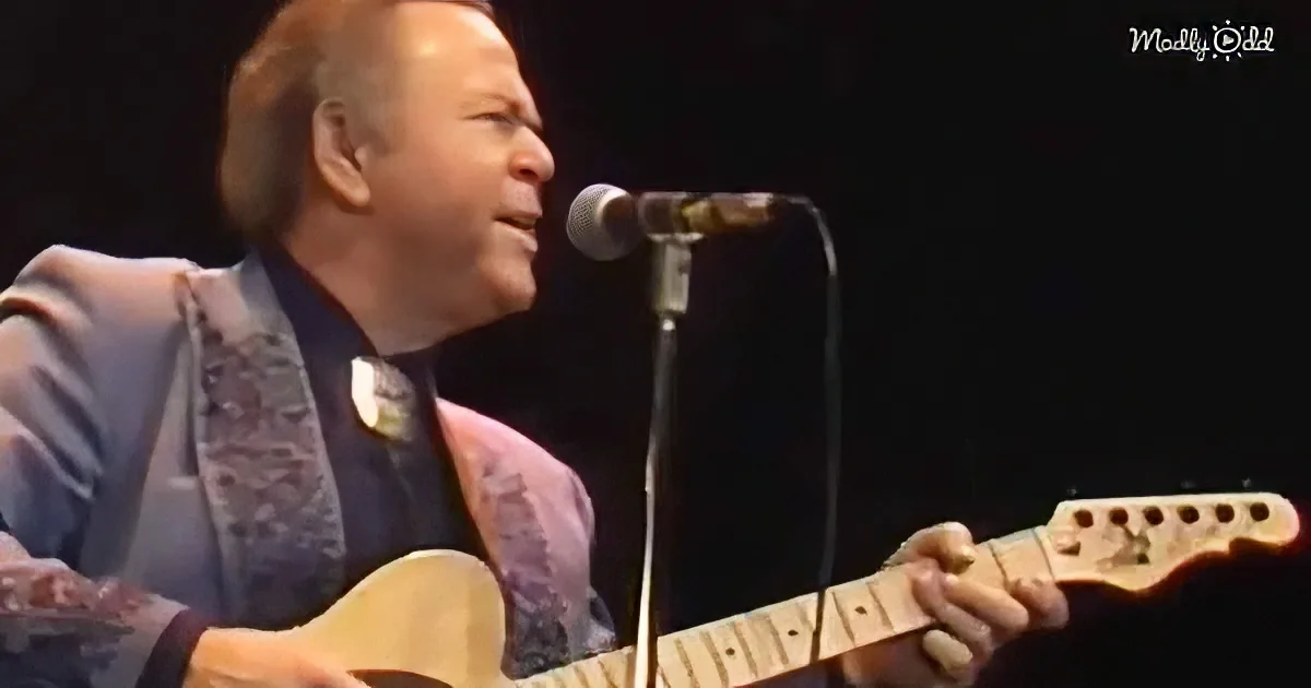 A man in a suit plays a guitar on stage, singing into a microphone.