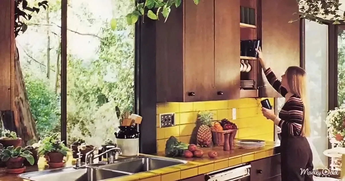 Woman reaches for item in wooden cabinet in retro kitchen with yellow tiles and greenery.