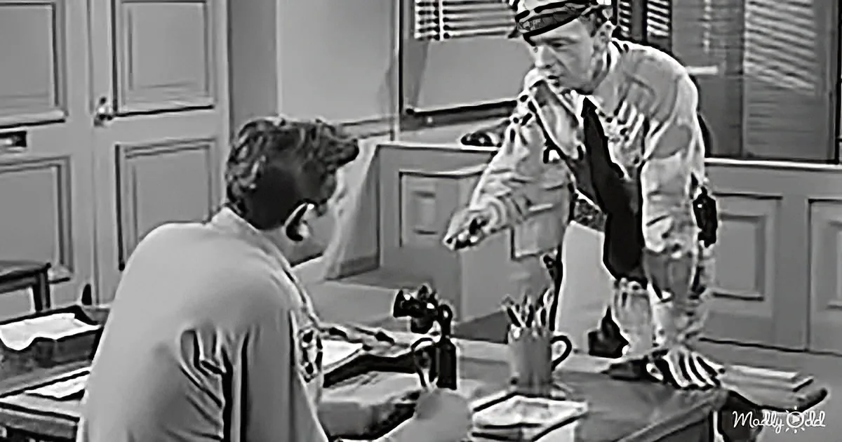 A man in a uniform leans over a table, gesturing towards a woman who is writing.