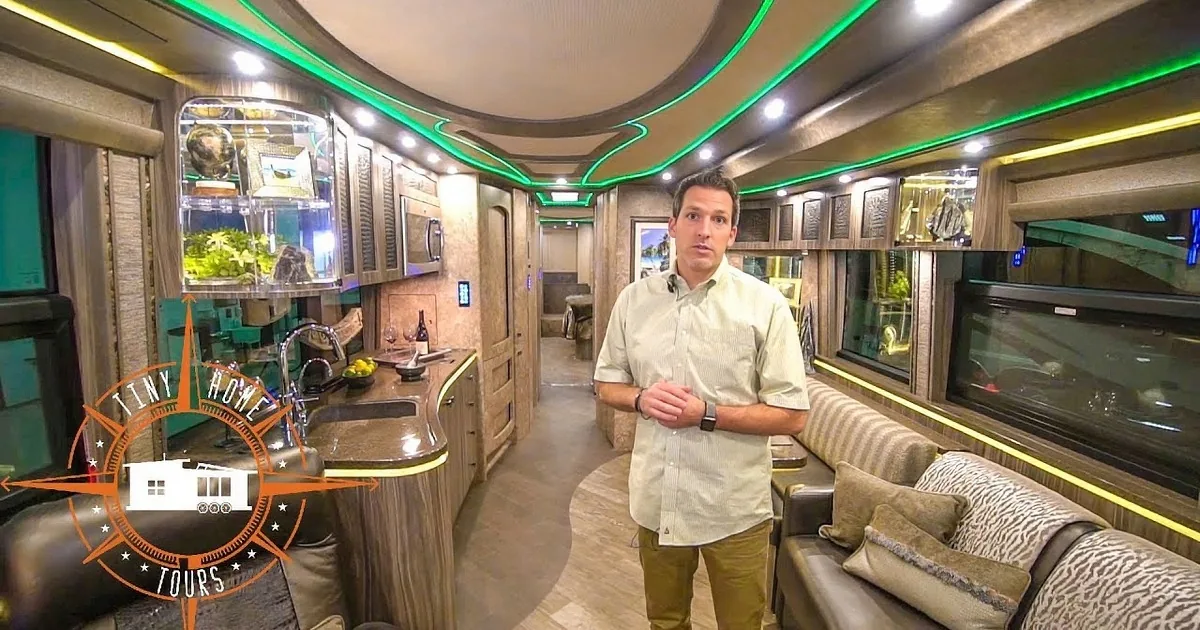 Man in white shirt gestures in modern RV kitchen with teal accents and LED lighting.