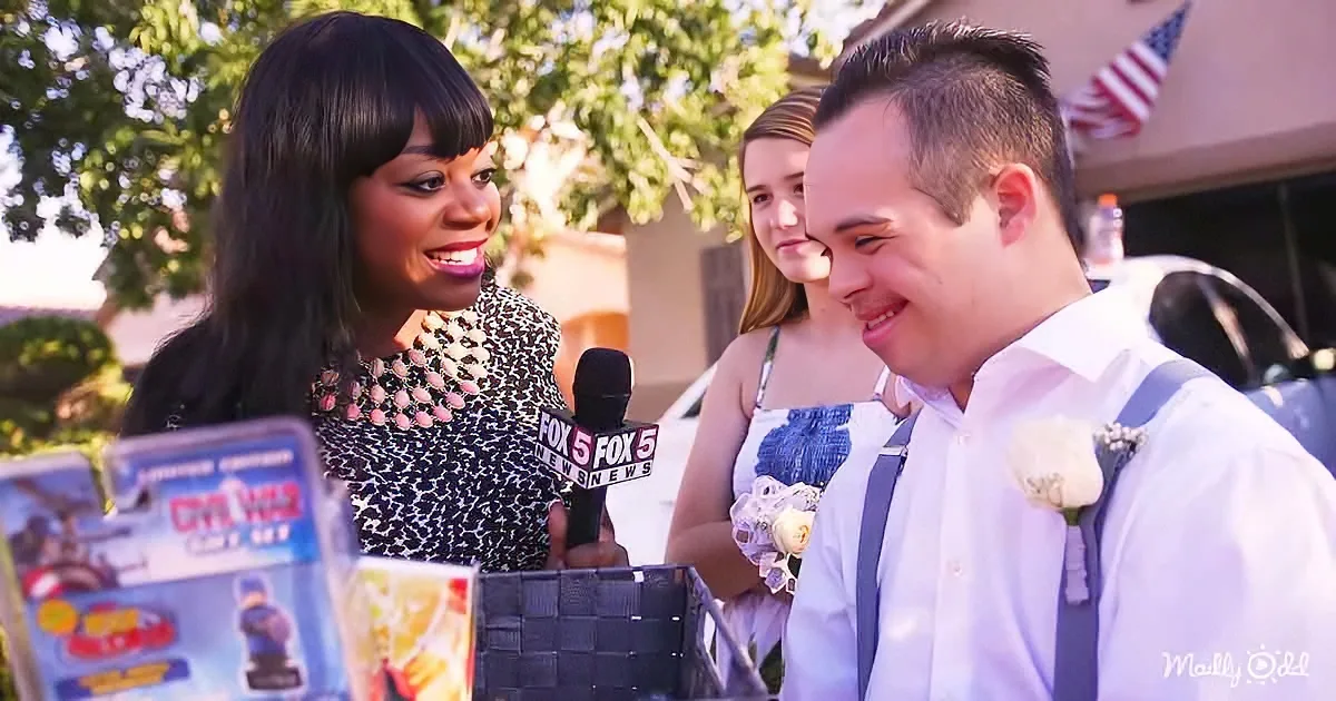 A woman in a leopard print dress holds a microphone, interviewing a man in a white shirt and suspenders at what appears...