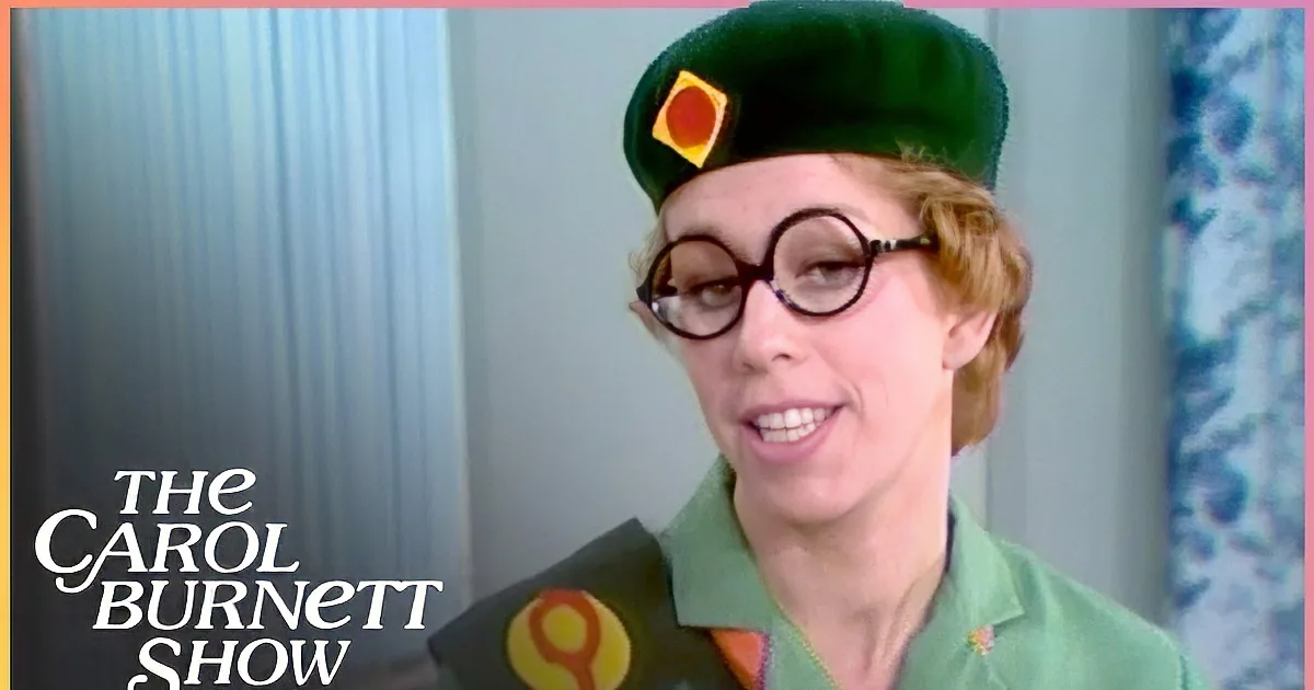 A person in a green uniform with a beret and glasses is speaking into a microphone.