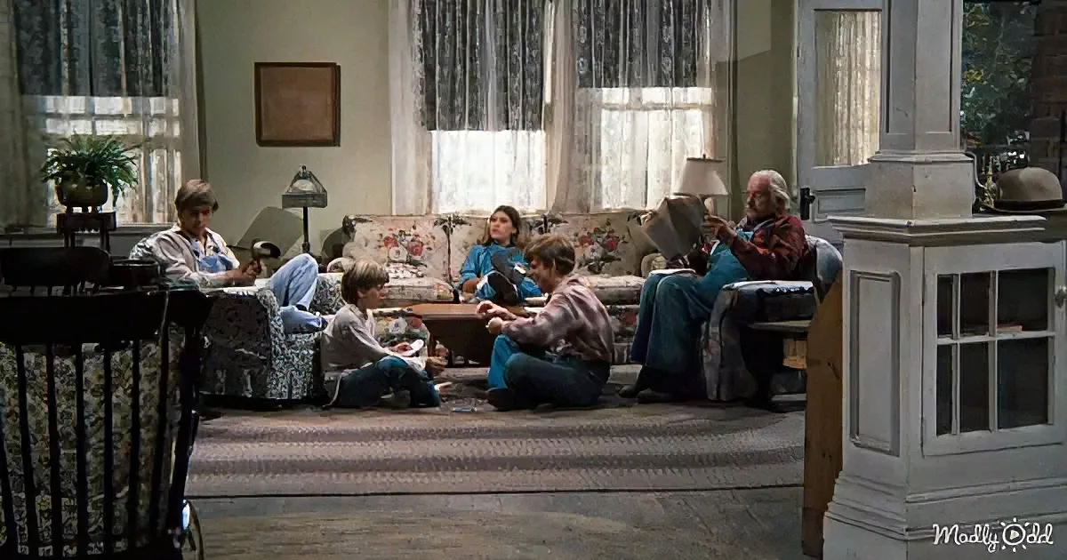 A family gathers in a cozy living room, engaging in various activities around a floral-patterned sofa.
