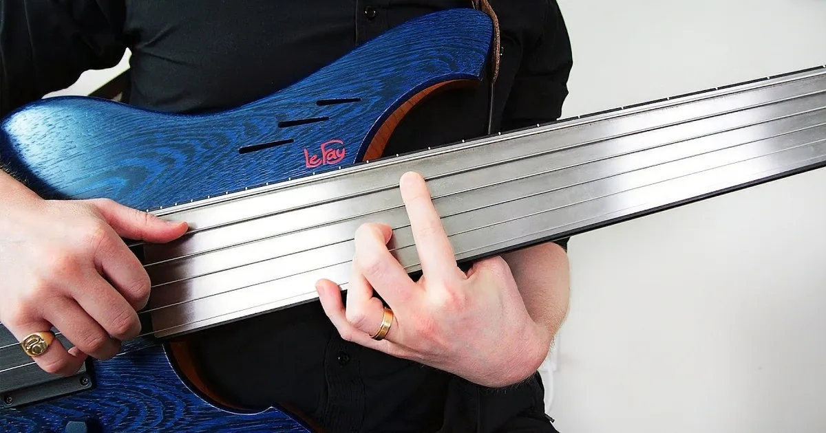 A person wearing headphones plays a six-string bass guitar, focusing intently on the instrument.
