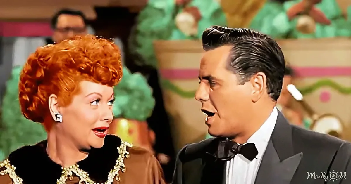 A woman with red hair and a man in a tuxedo are in a colorful, festive setting.