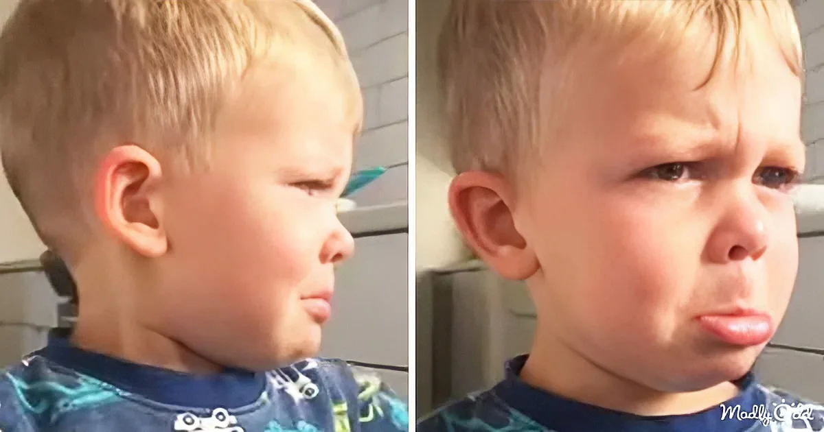 A young boy with blonde hair wearing a blue shirt looks to the side, showing his profile and slightly puffed cheeks.