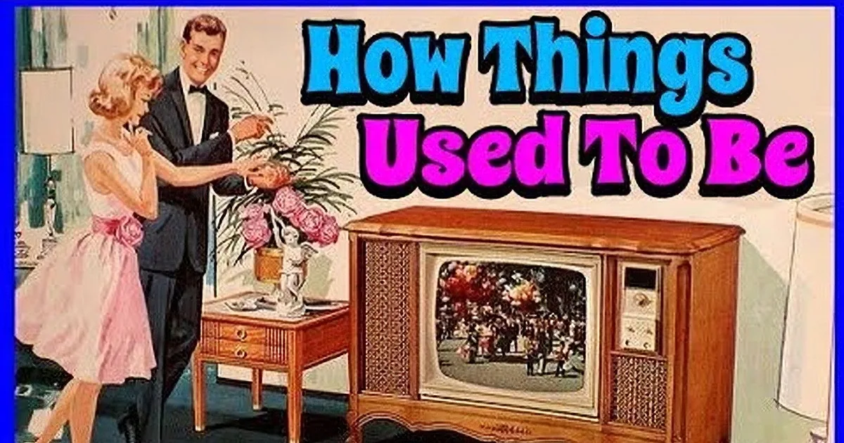 A man in a suit points at a television while a woman stands beside him, another man sits on a TV set.