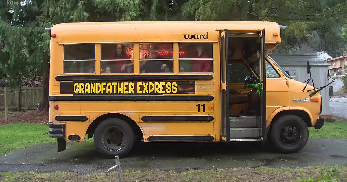 A man in a Santa hat stands with children in front of a decorated school bus, celebrating Christmas.