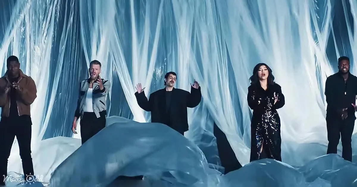 A group of performers stands on a stage with a backdrop of draped, icy blue fabric, creating a cold, ethereal atmosphere.