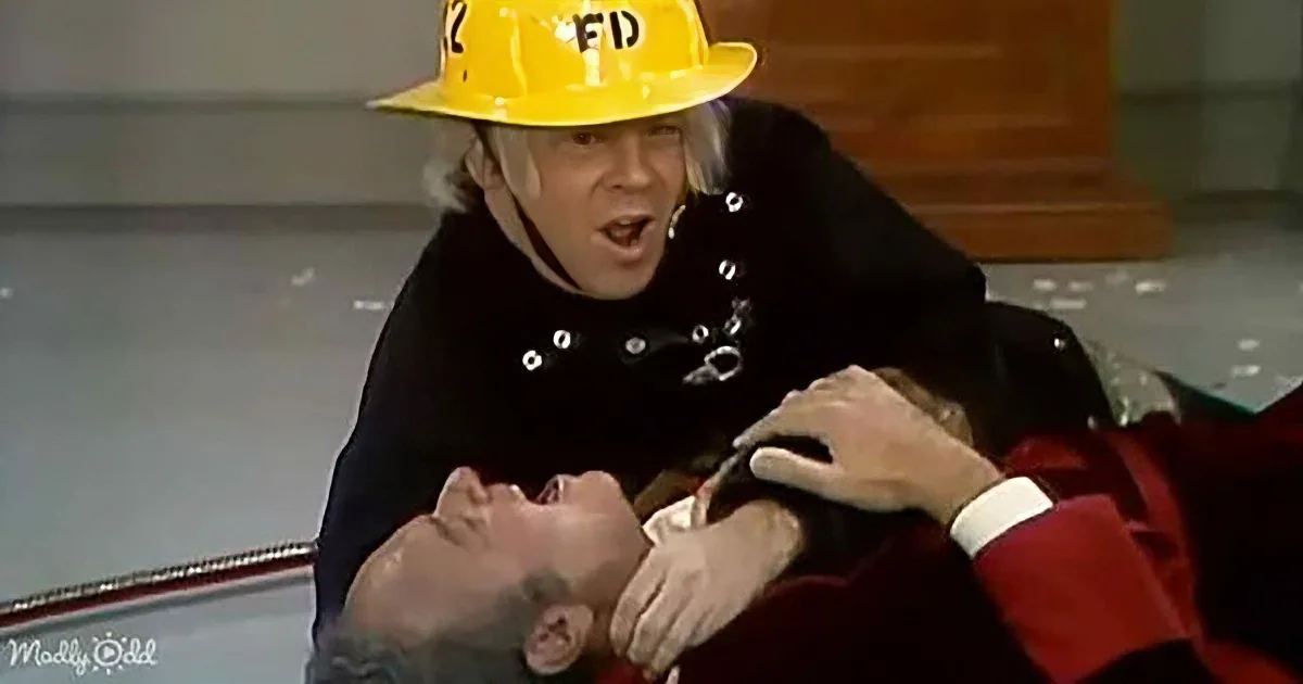 A firefighter in a yellow helmet and black jacket is assisting a person in a red jacket, who appears to be unconscious.