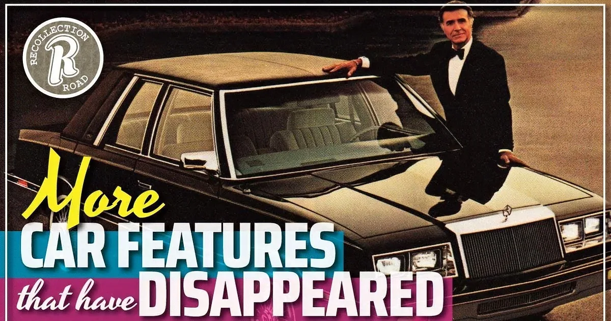 A man stands beside a classic black car with a tan interior, parked on a brick driveway.