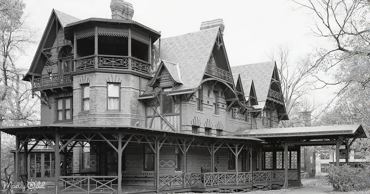 A Victorian-style house with intricate woodwork and a wrap-around porch stands amidst bare trees.