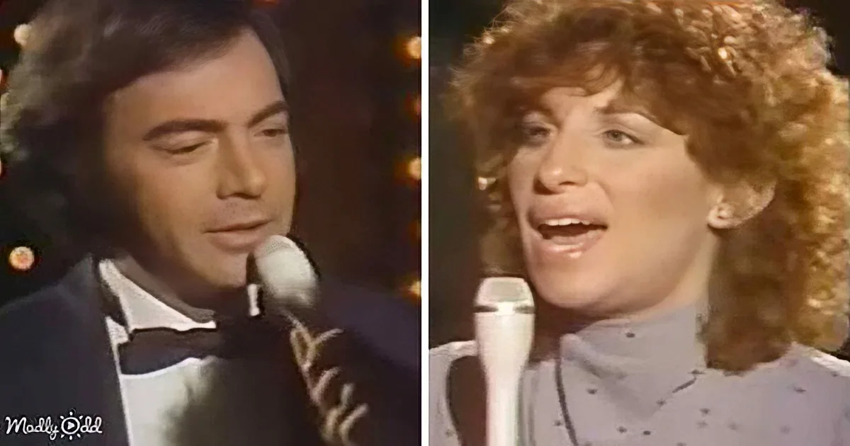 A man in a tuxedo and a woman with curly hair sing into microphones, likely performing on stage.